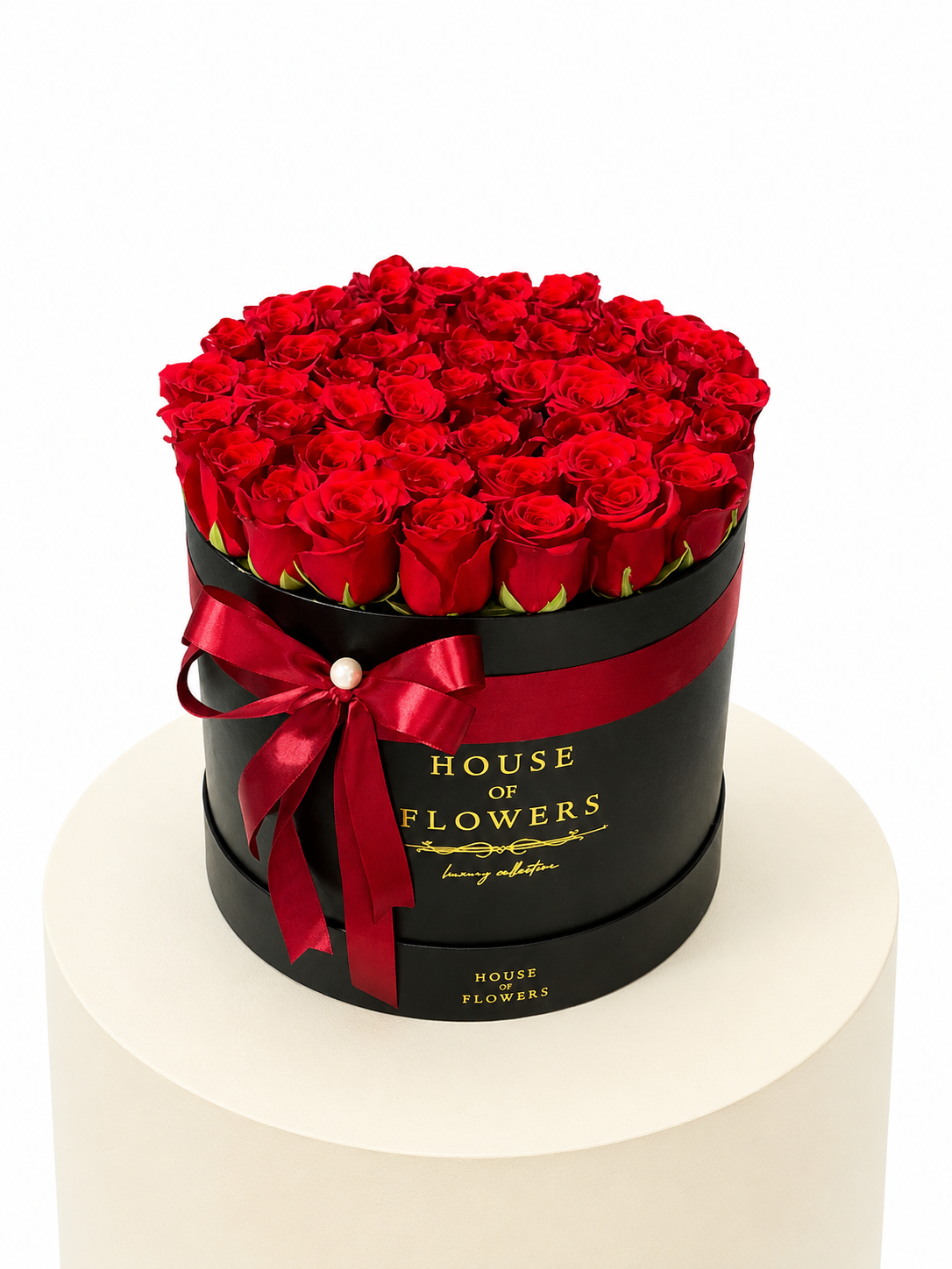 A round black gift box filled with red roses, tied with a red ribbon and featuring gold &