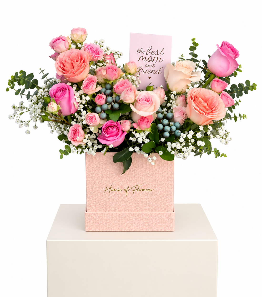 A floral gift arrangement in a pink box from House of Flowers, featuring pink and peach roses, green foliage, small white flowers, blue berries, and a card that reads &