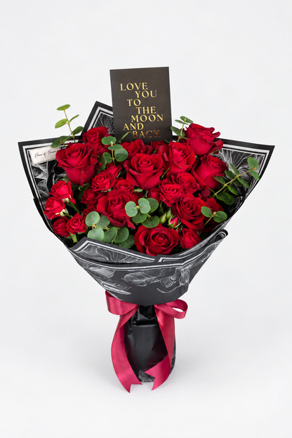 Ruby Woo bouquet of red roses and eucalyptus wrapped in black patterned paper with a red ribbon and "Love You to the Moon and Back" card