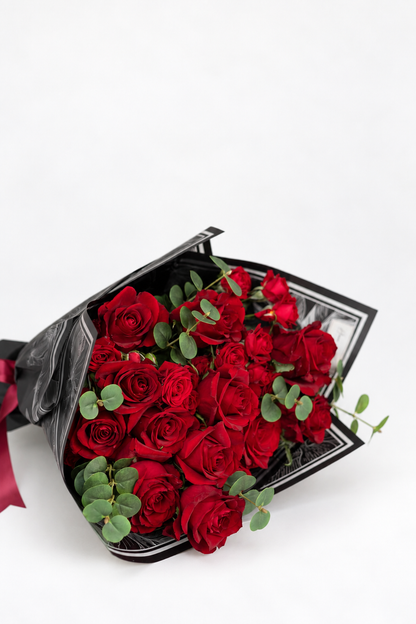 Ruby Woo bouquet of red roses and eucalyptus wrapped in black patterned paper with a red ribbon and "Love You to the Moon and Back" card