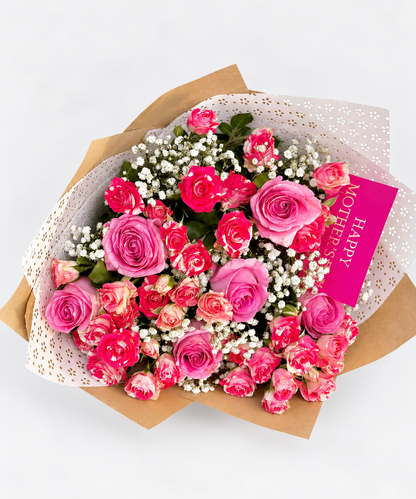 Timeless Tribute bouquet with pink and hot pink roses and gypsophila, wrapped in kraft and white paper with a pink ribbon and card