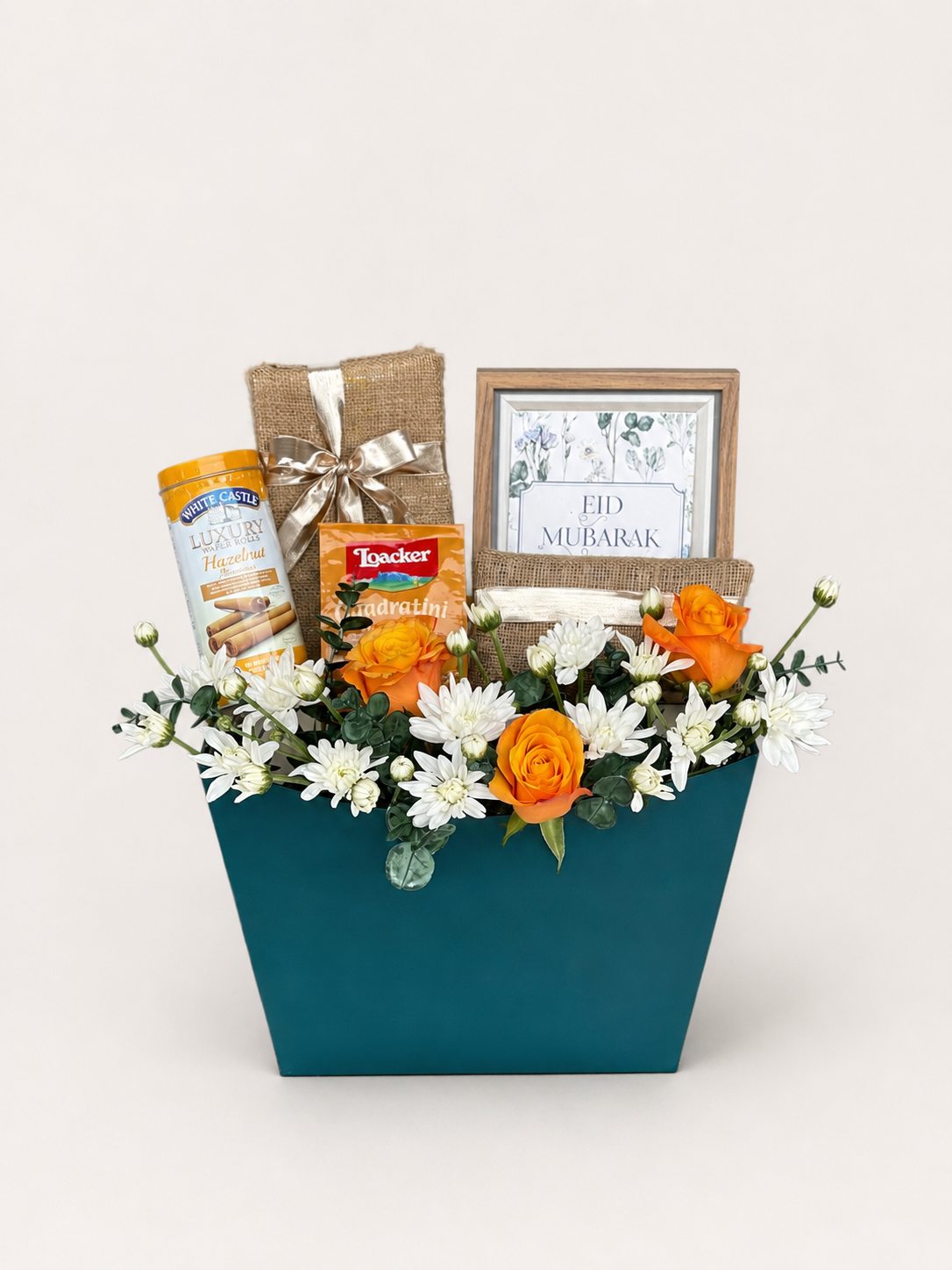 House of Flowers Eid ul Adha Treats gift box in a teal box with orange roses, white chrysanthemums, White Castle Luxury Hazelnut wafers, Loacker wafers, jute-wrapped gift, and an Eid Mubarak framed card