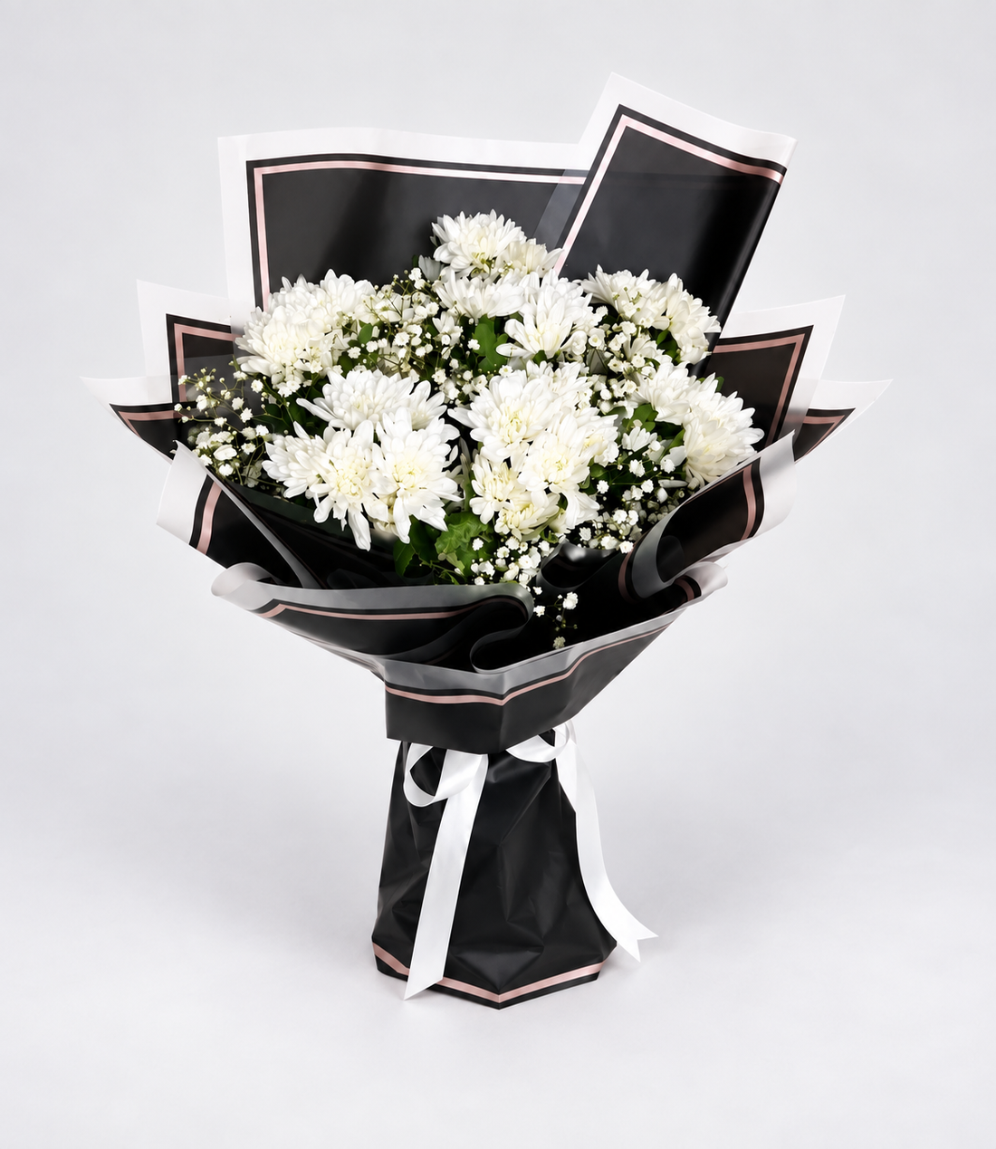 A bouquet of white chrysanthemums wrapped in black paper with white ribbon accents, displayed on a light beige pedestal against a white background.
