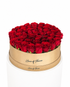 A round gift box filled with preserved red roses, wrapped in a metallic gold band printed with &